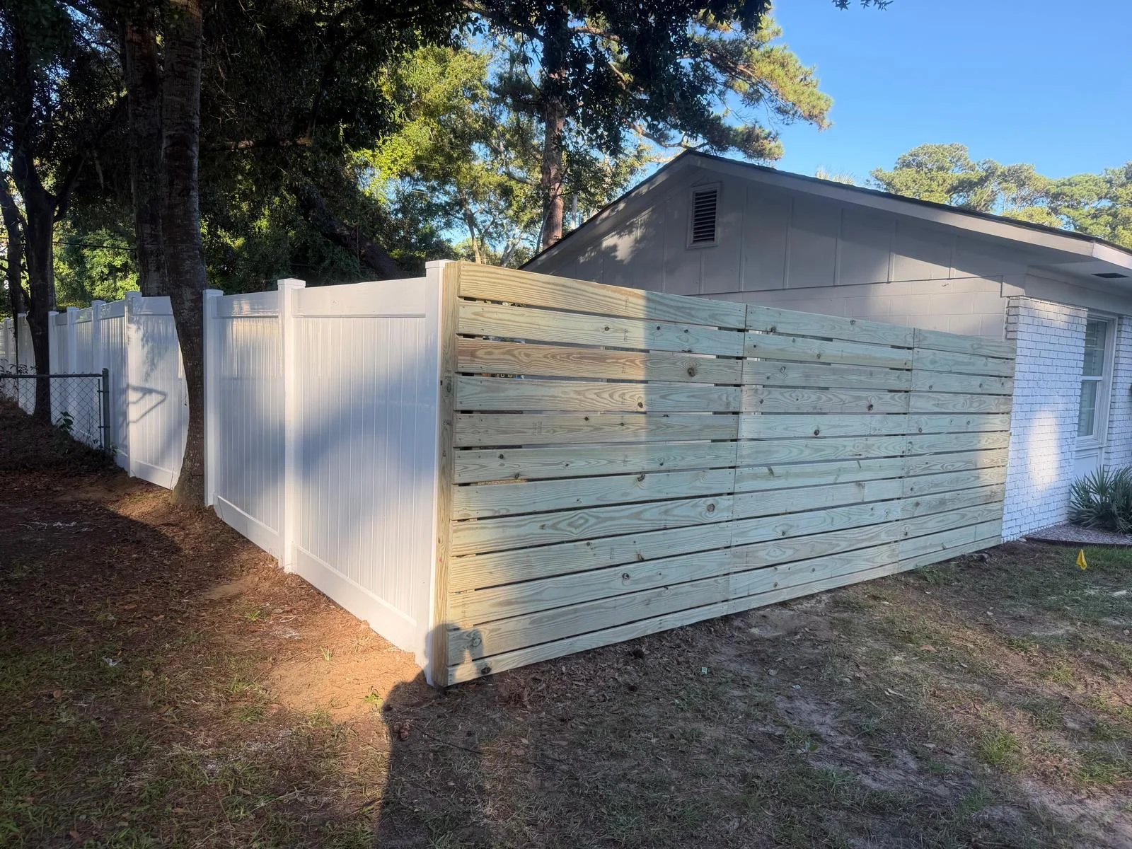 Horizontal wood fencing transitioning to white vinyl beside a home