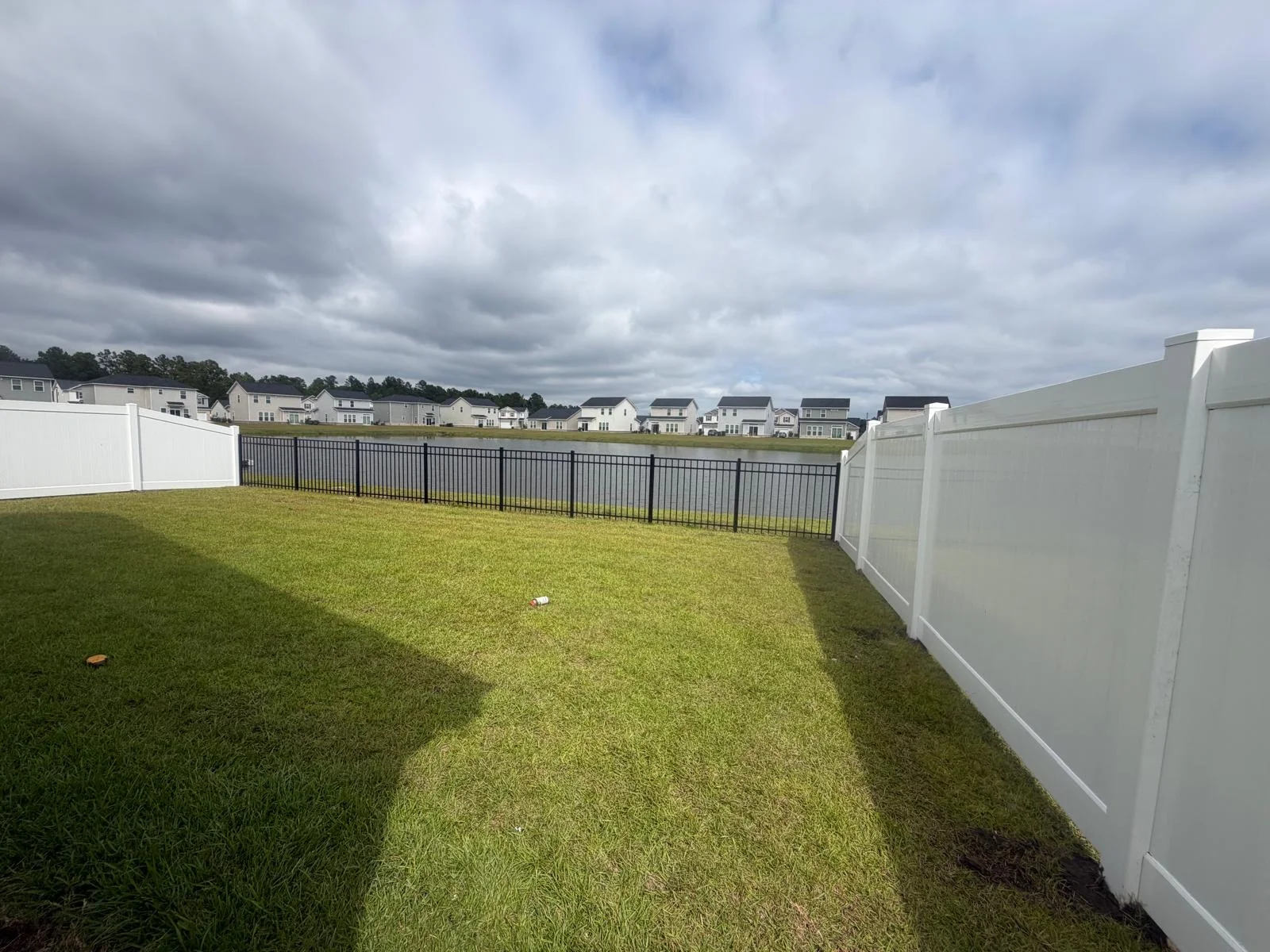 Backyard enclosed by white vinyl and black aluminum fencing