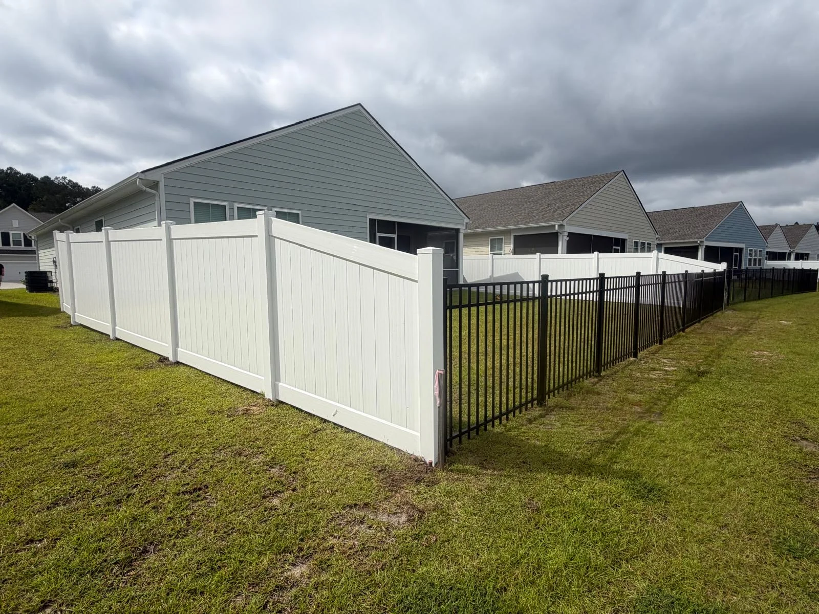 White vinyl privacy fence meeting an open black aluminum fence