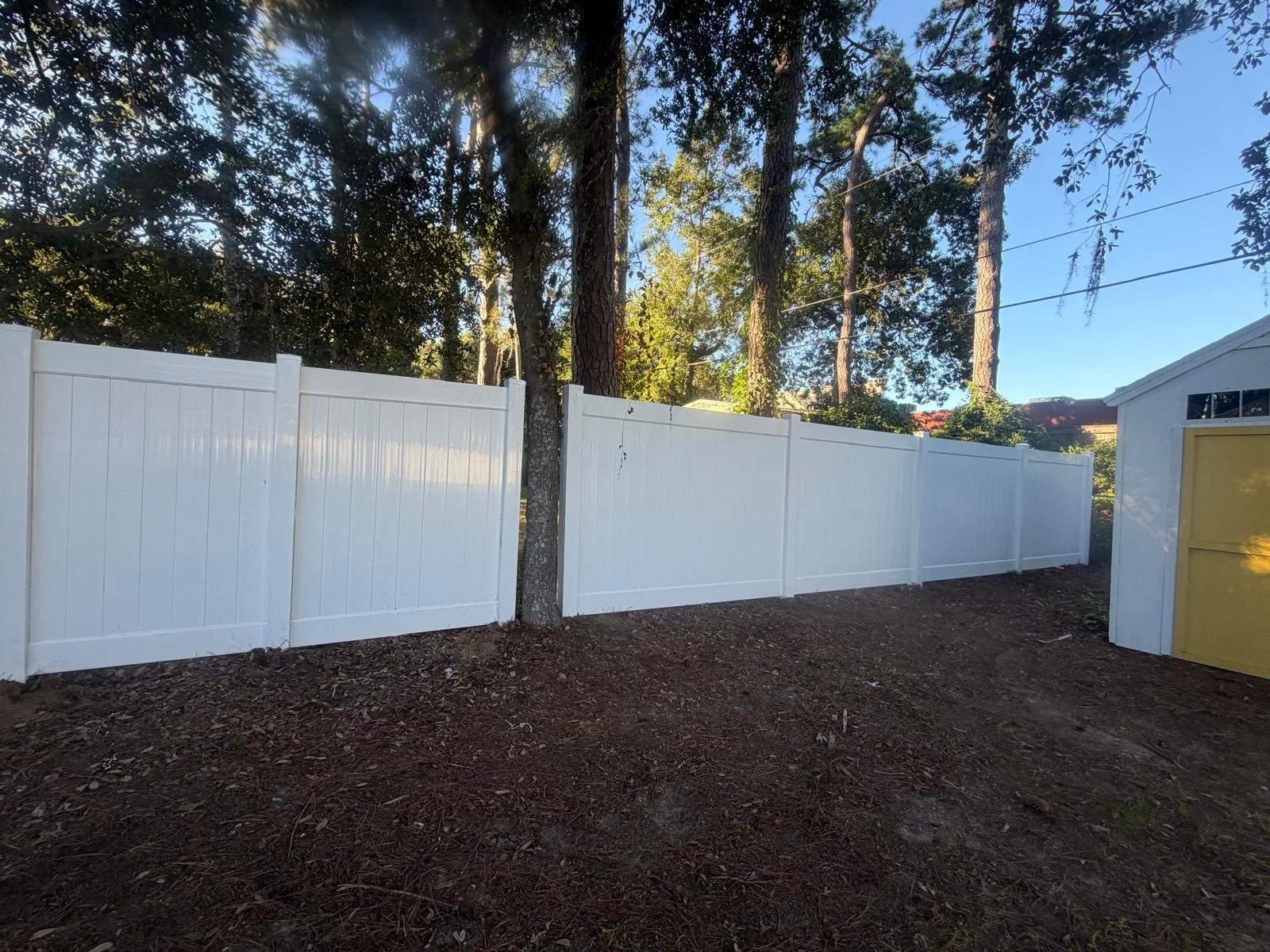 White vinyl privacy fence along a wooded backyard